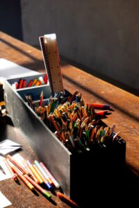 A close-up of a sunlit desk with colorful pencils in a black holder, creating an artistic atmosphere.