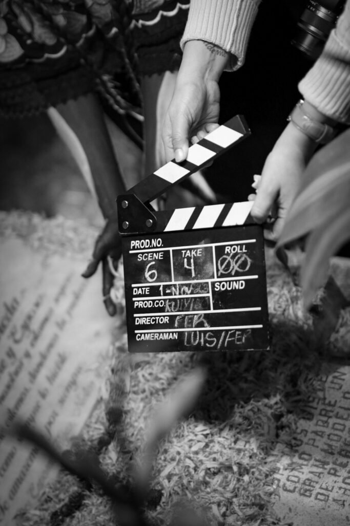 Black and white photo of hands holding a clapperboard on a film set, capturing cinematic action.
